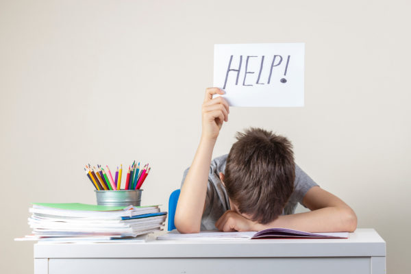 Child working on homework puts up a sign with the word "HELP!" written on it.